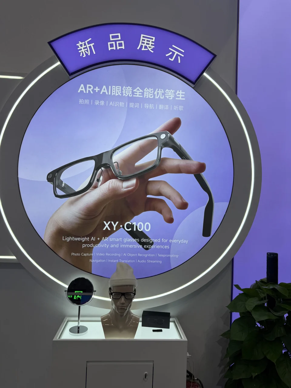 C100 glasses display with a purple circular product poster and a mannequin wearing glasses