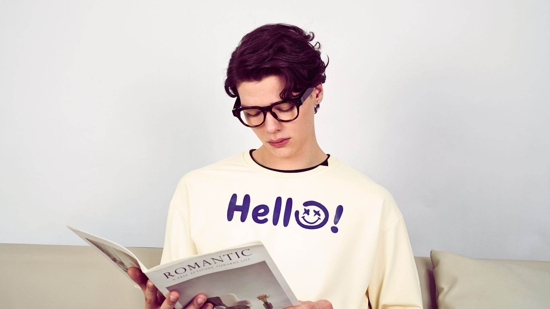 Model wearing tortoiseshell K900 camera-and-audio smart glasses while reading at home